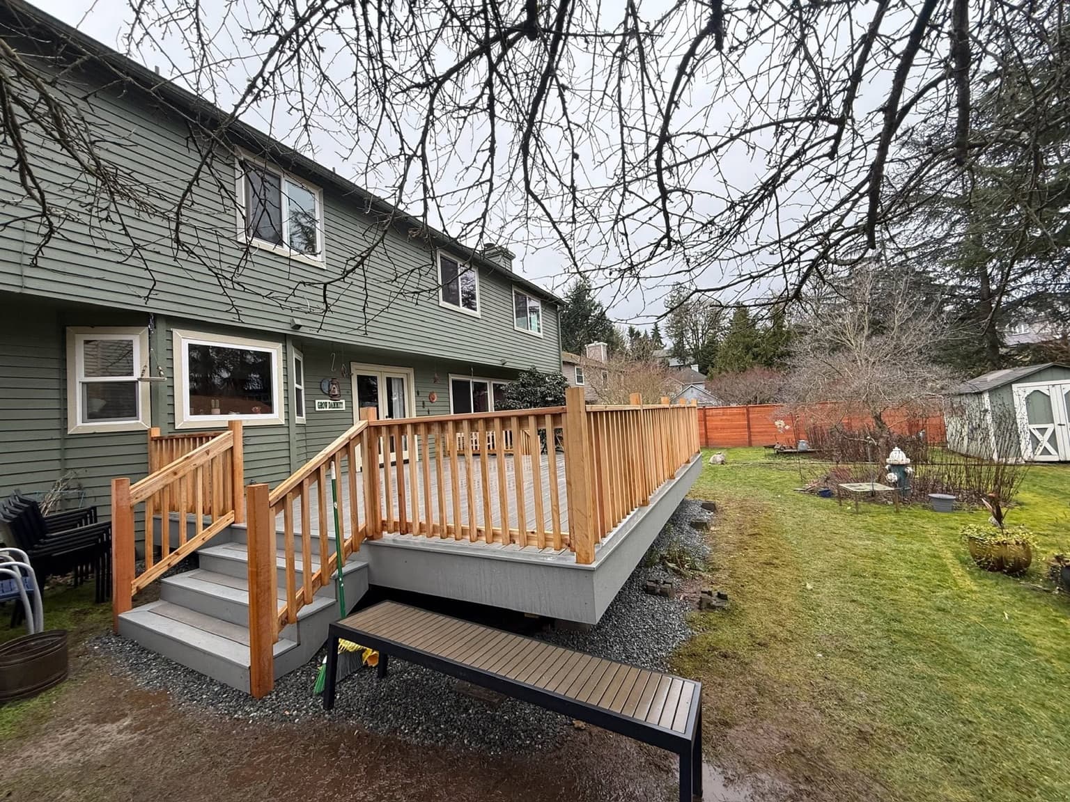Raised composite deck with cedar railing and balusters and a stair run down to a gravel base
